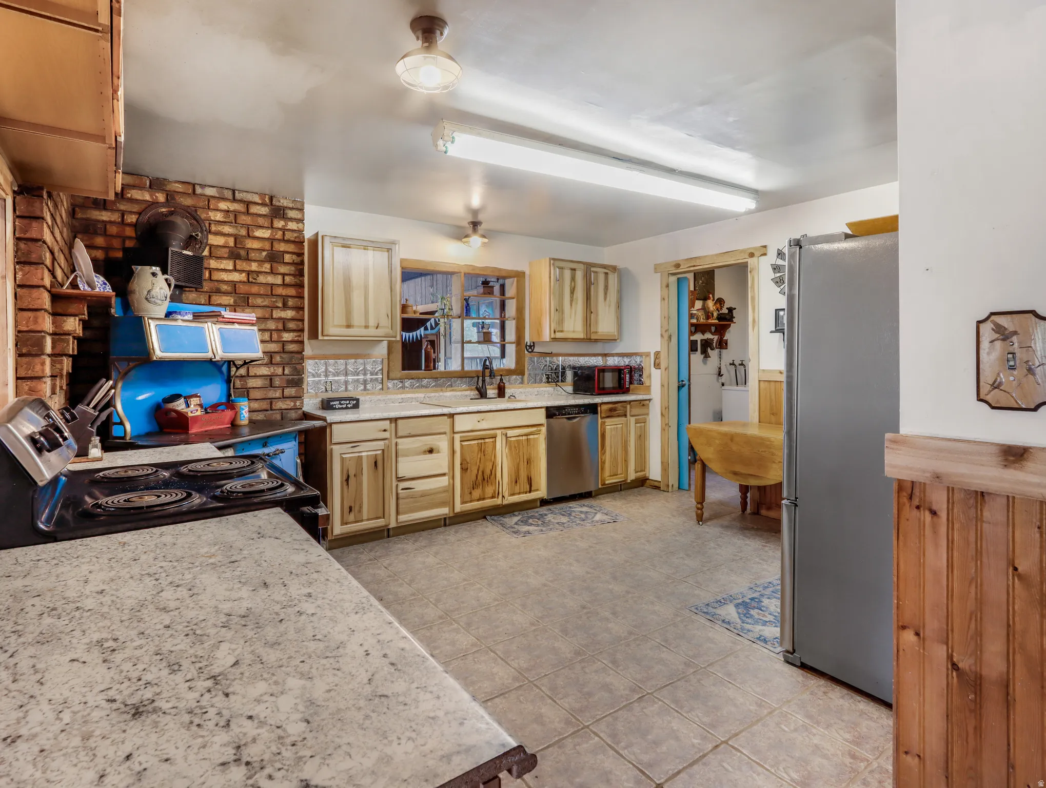 Kitchen featuring a tiled floor, wood-finish cabinetry, light-toned countertops, and a brick accent wall