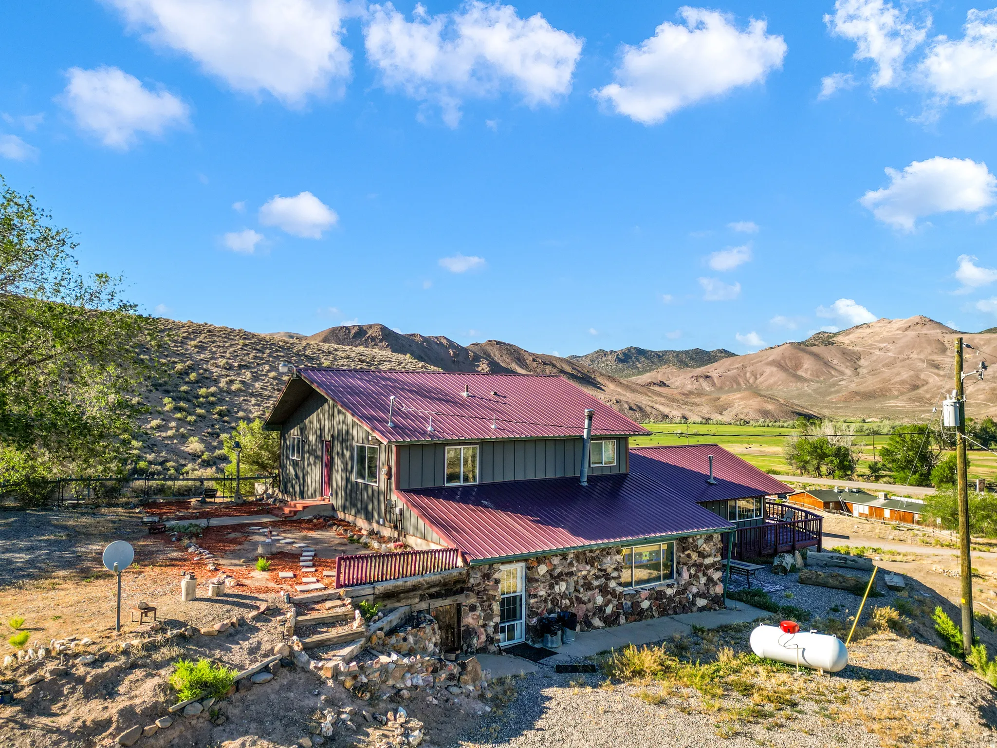 Stone and siding exterior with a red metal roof, featuring multiple decks and a terraced landscape