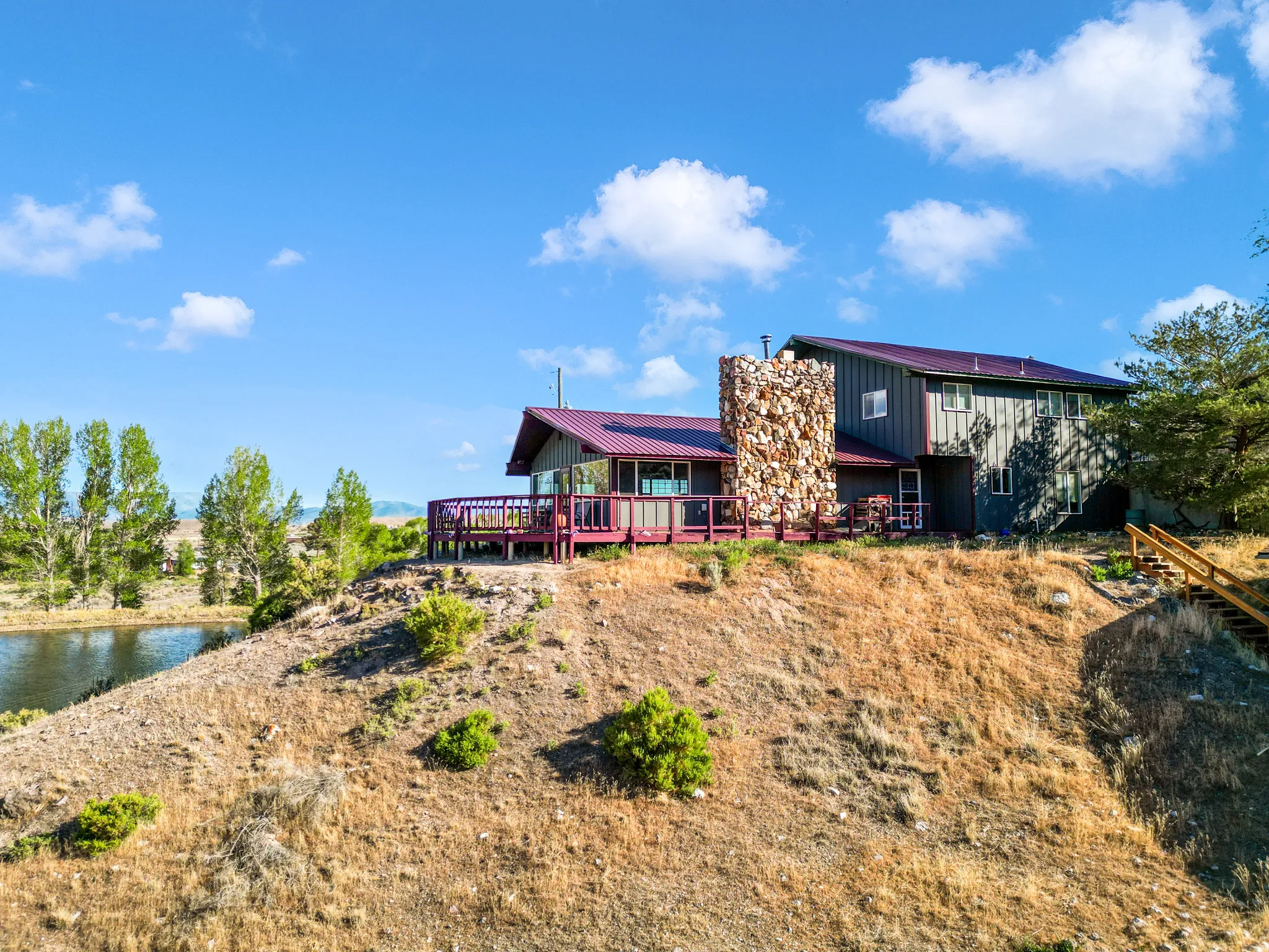 Multi-level residence featuring a metal roof, an expansive outdoor deck, and a stone-clad chimney