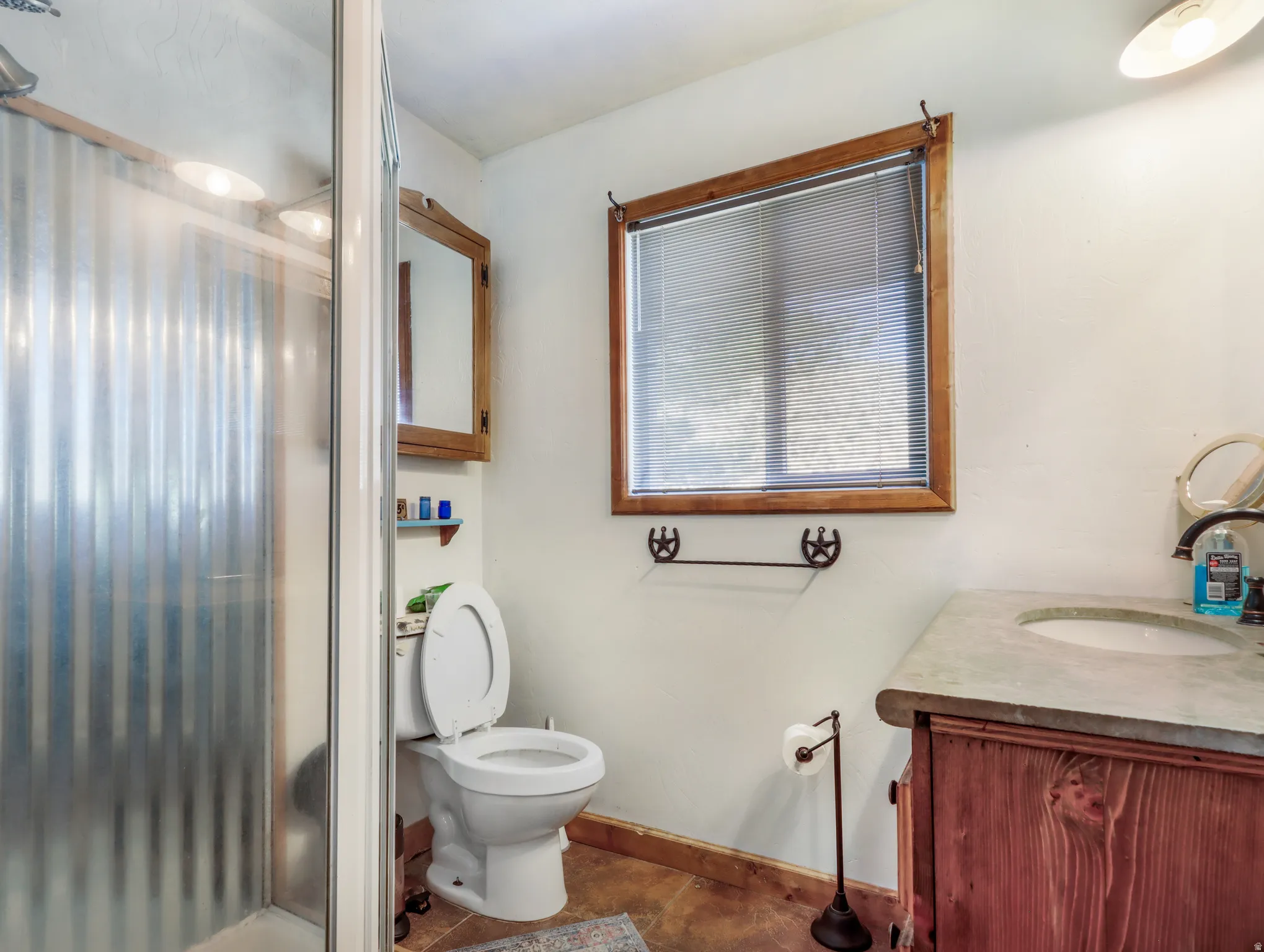 Walk-in shower with corrugated paneling, wood-framed window with blinds, wood-finish vanity with an integrated sink, and wood-finish flooring