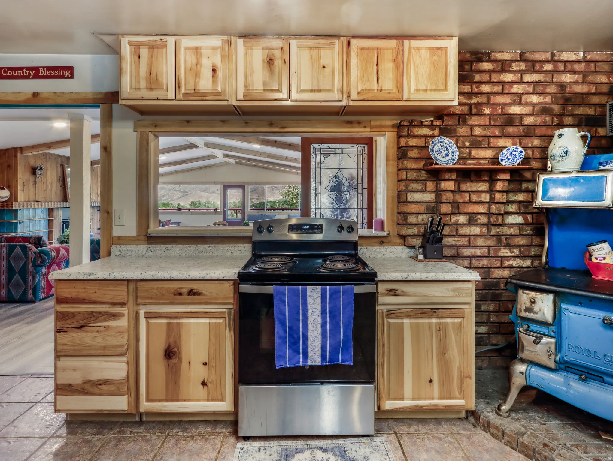 Light wood-finish cabinetry, light-toned countertops, tile flooring, and exposed brick wall detailing