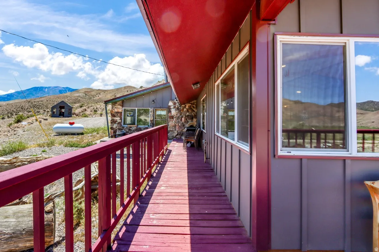Wraparound wood deck with red railings and overhead covering, vertical plank siding, and multiple windows