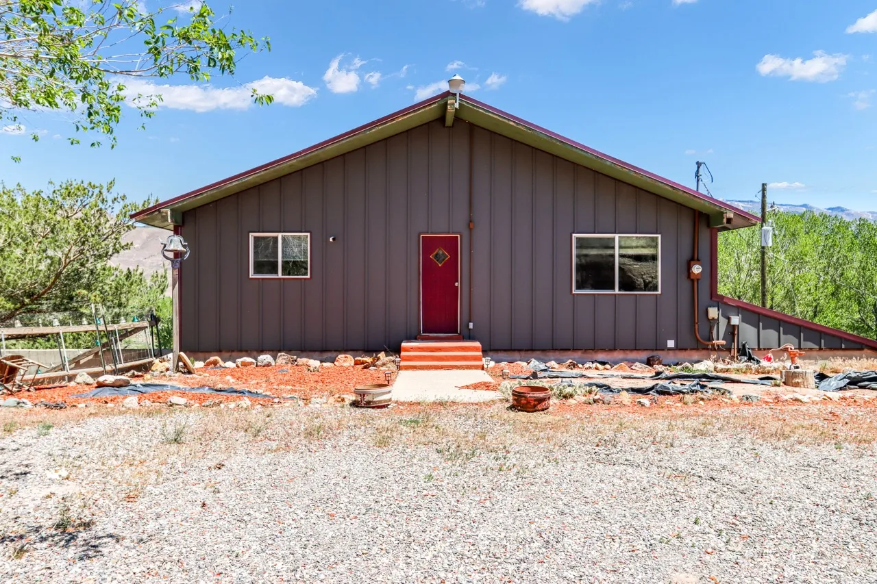 Gable roofline with wide eaves, vertical panel siding, and a vibrant red entry door