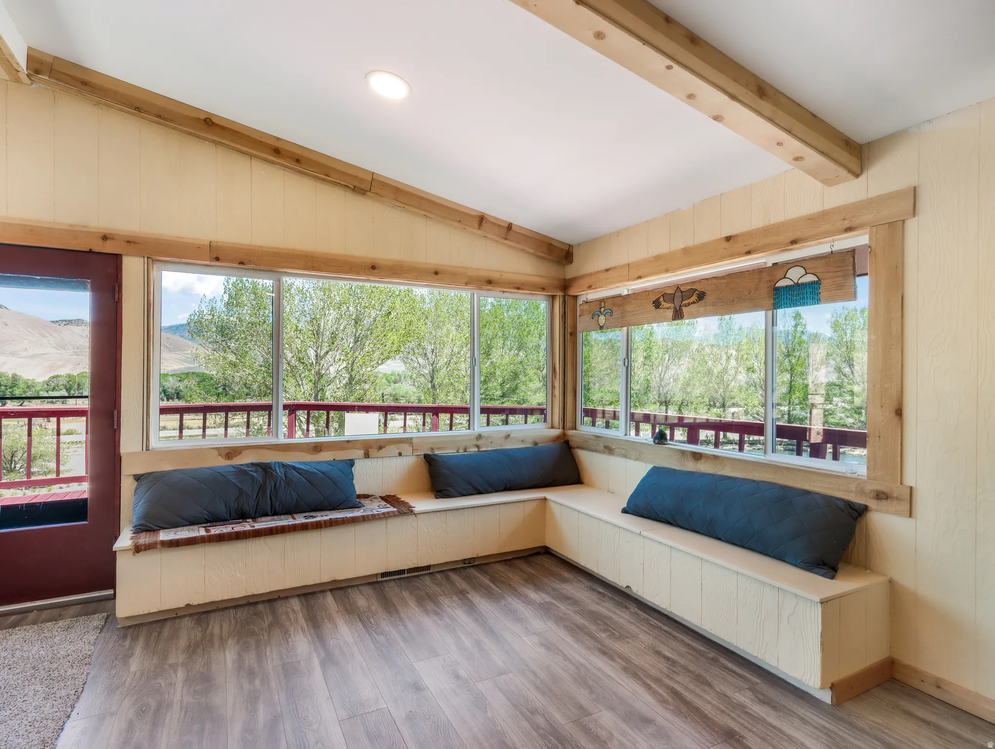 Expansive window wall, wood-finish flooring, built-in bench seating, wood-beamed ceiling, and recessed lighting