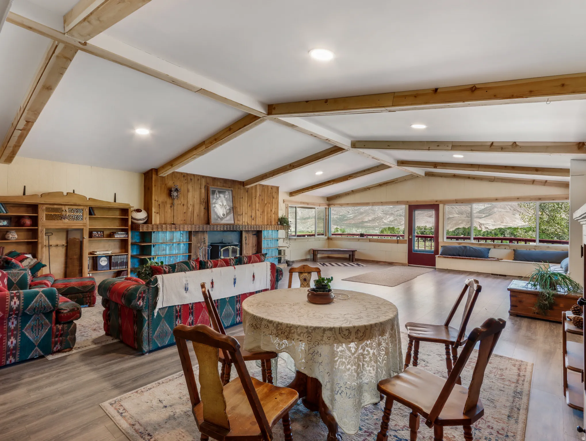 Vaulted ceiling with exposed wood beams, wood-finish flooring, wood-paneled wall, built-in shelving, and a prominent fireplace with a tiled hearth