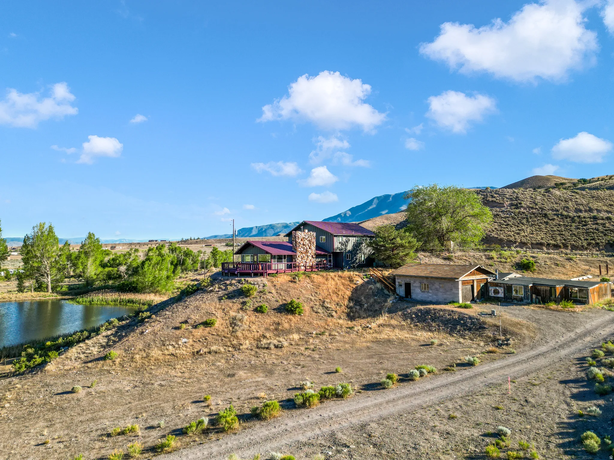 Expansive property featuring a main residence with a stone facade, an elevated deck, and a distinct red roof