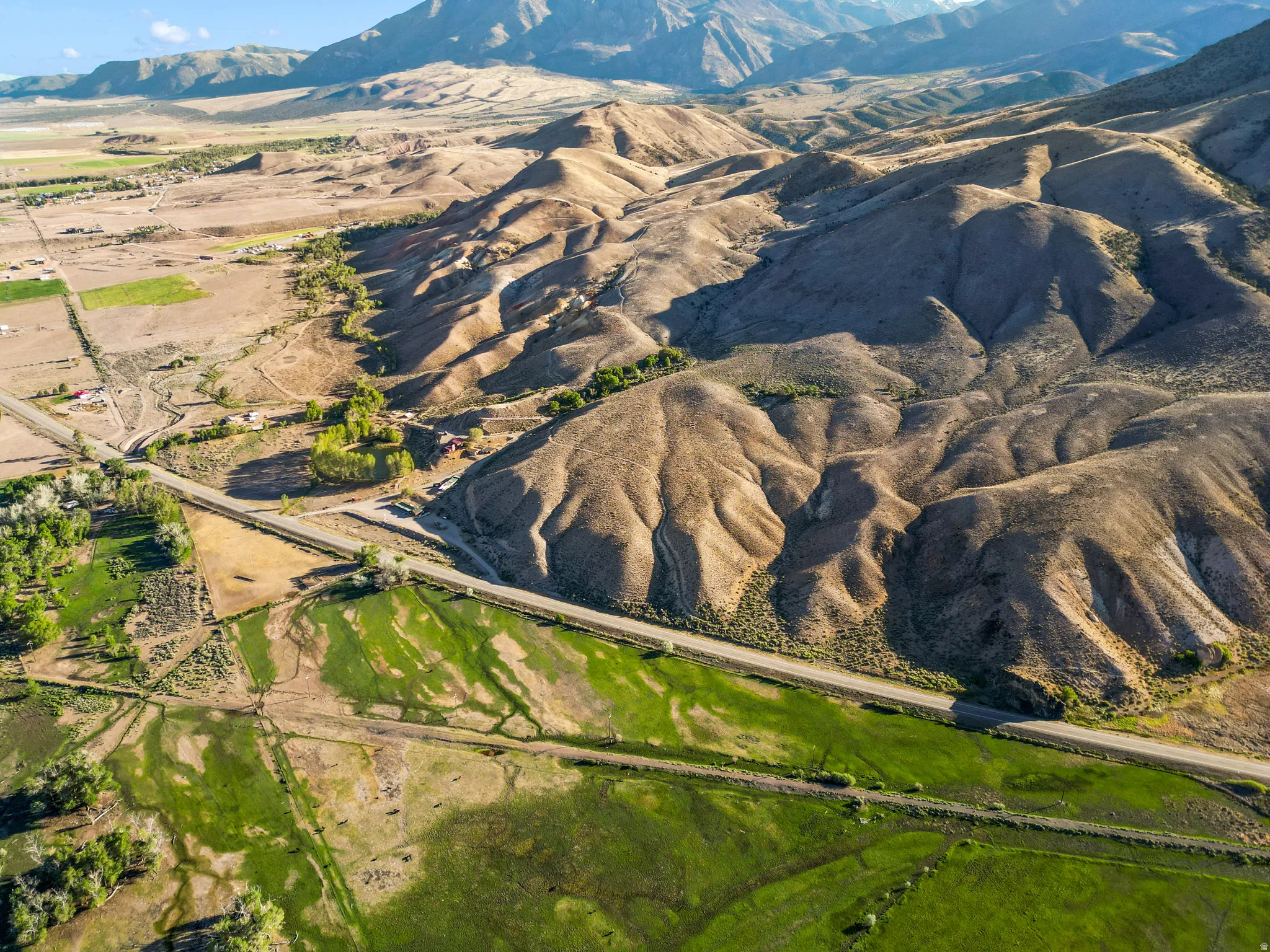 Expansive landscape featuring rolling hills, a winding roadway, diverse terrain, verdant fields, and distant mountains