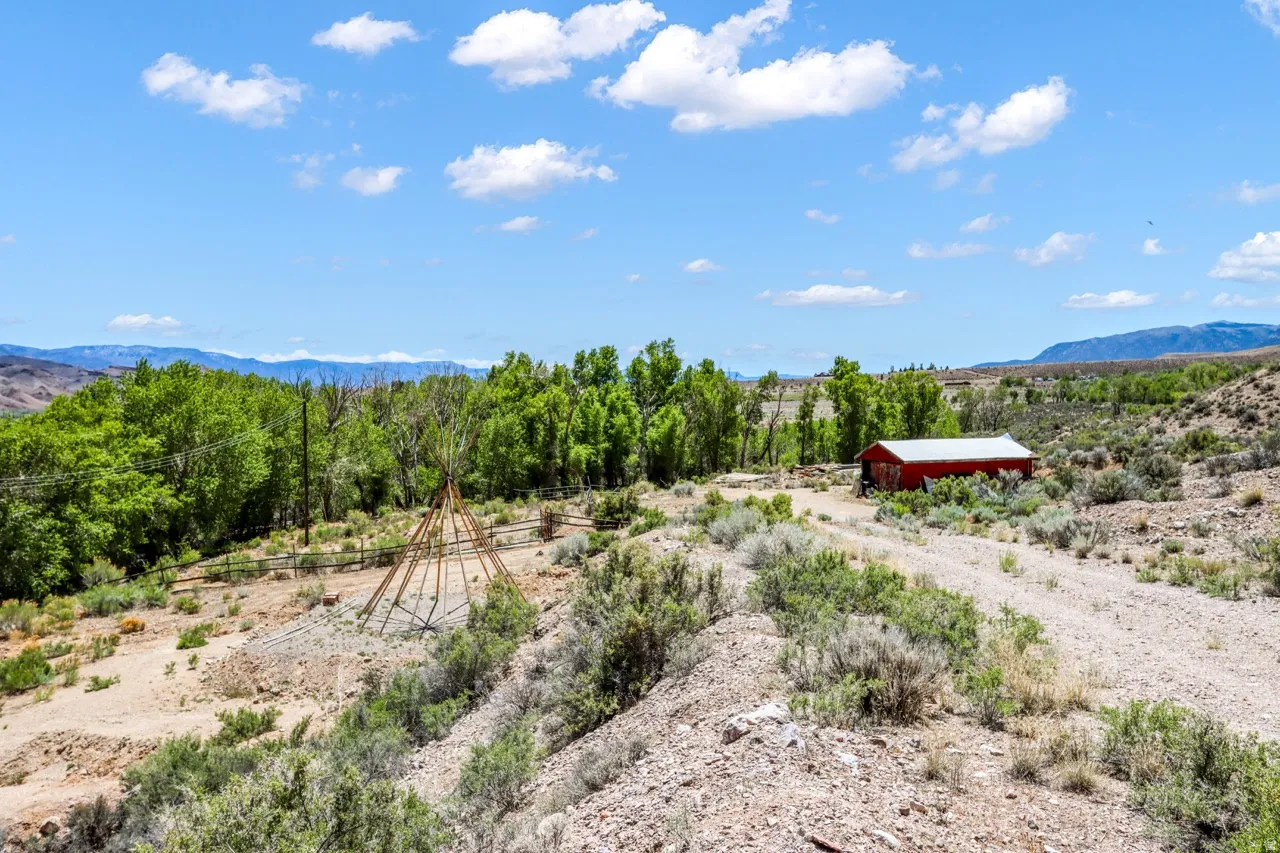 Expansive property featuring a red barn structure, mature trees, mountain range backdrop, and natural landscaping