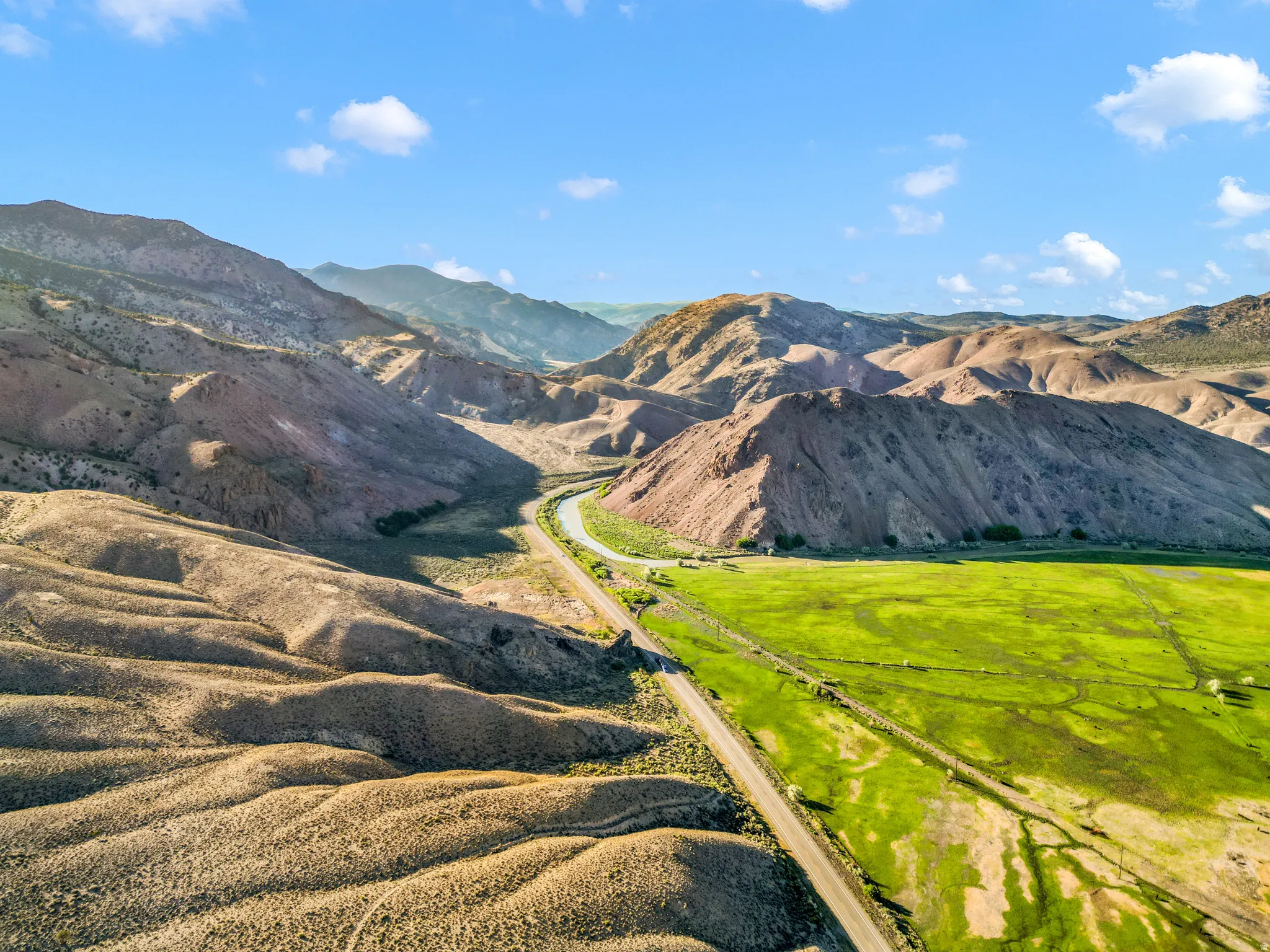 Expansive green field, natural mountainous terrain, and a winding road