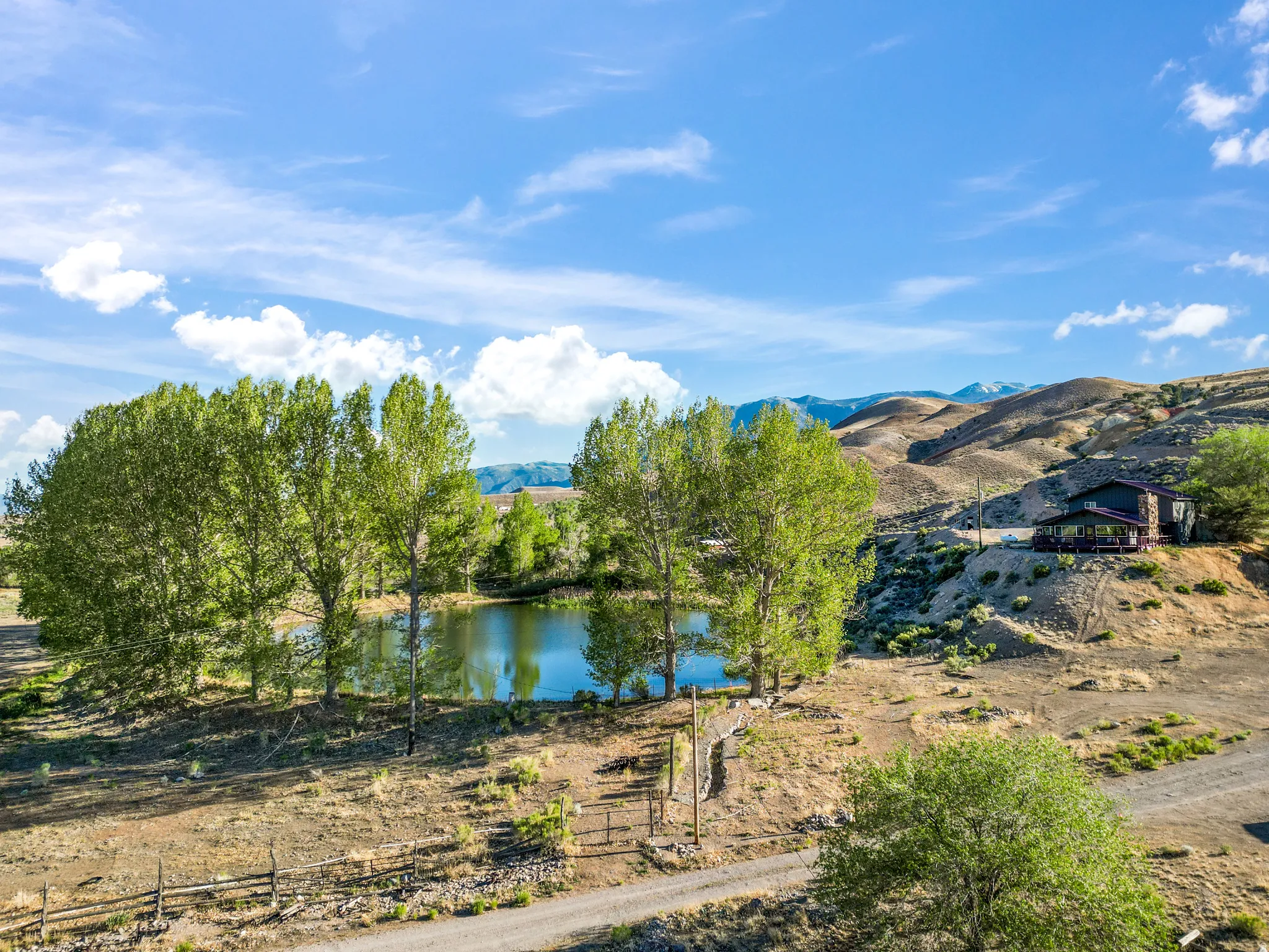 Expansive property featuring a private pond, mature trees, and a dwelling with an exterior deck