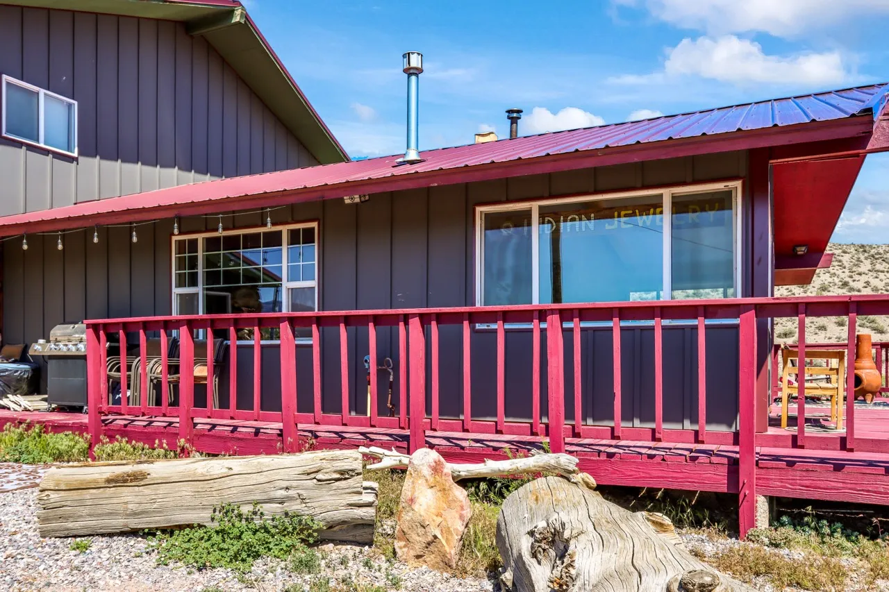 Exterior featuring gray vertical siding, a red metal roof, and a red-painted wooden deck