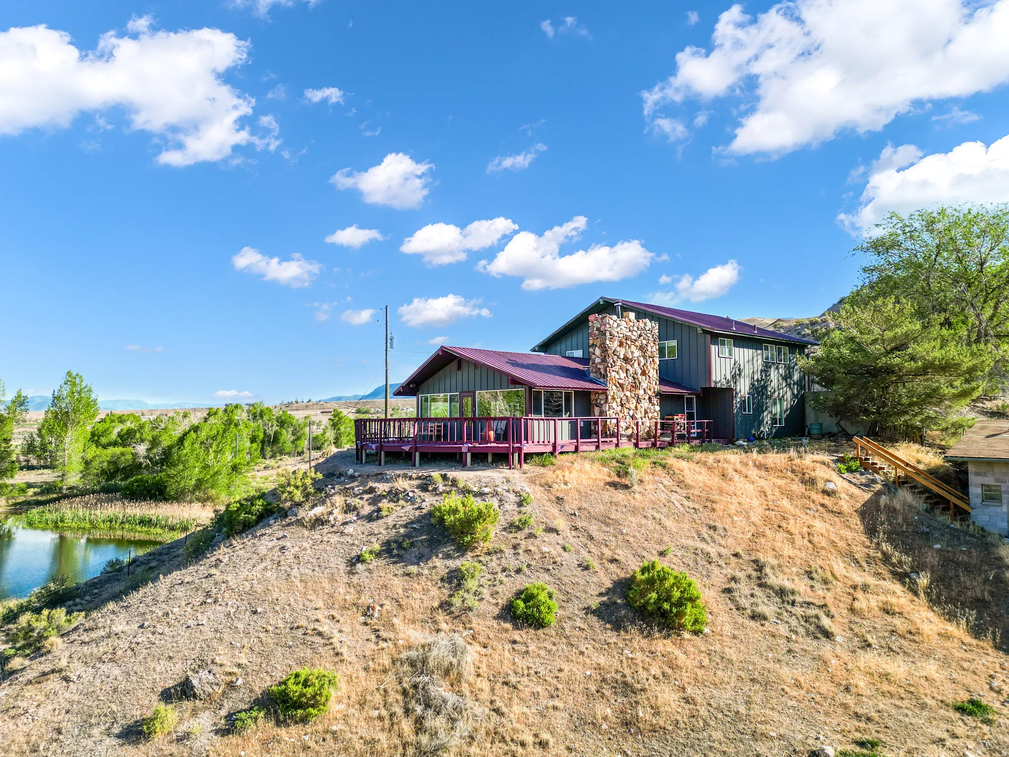Exterior with a stone chimney, a red outdoor deck, and an adjacent pond