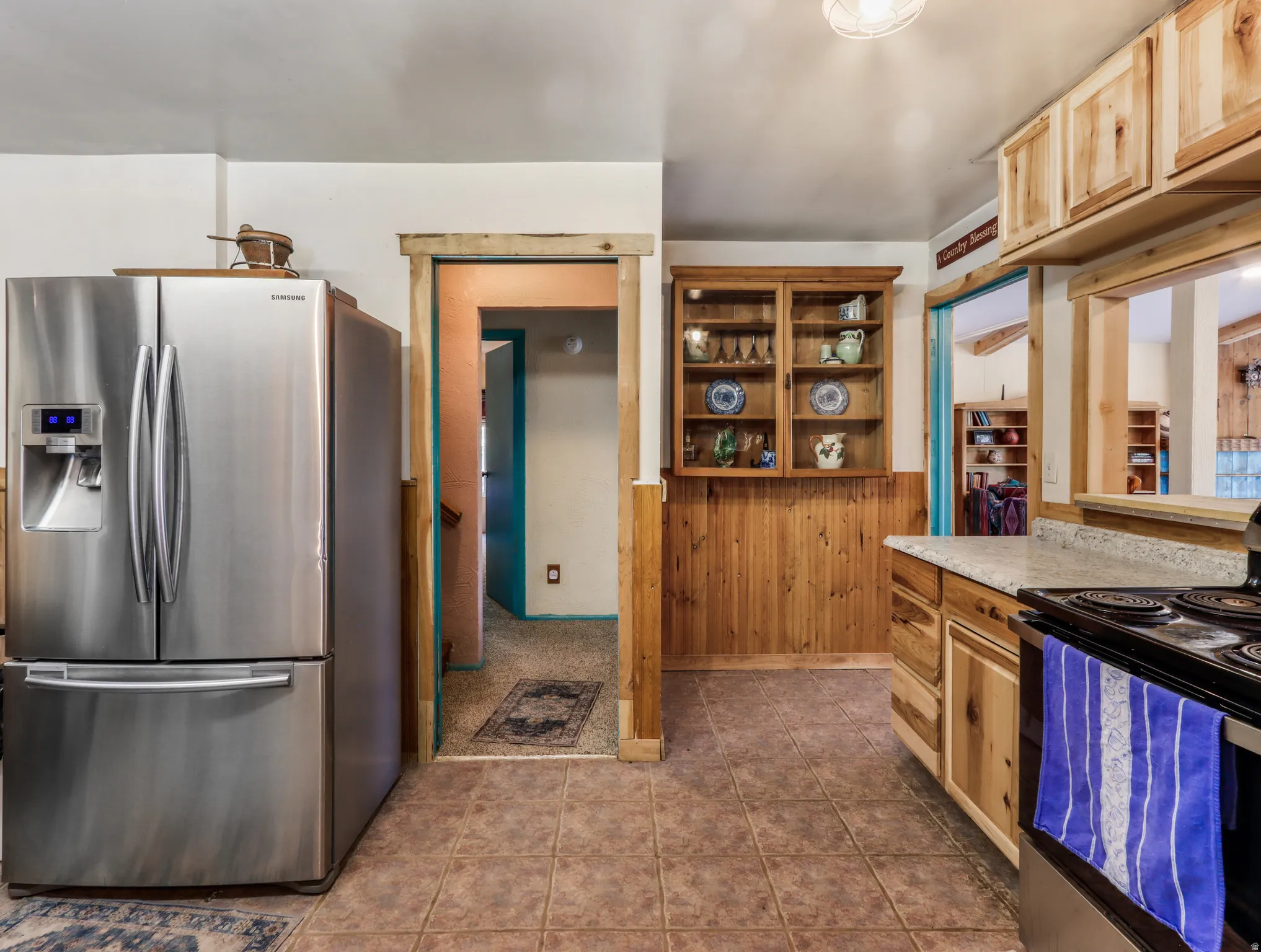 Stainless steel refrigerator, tile flooring, wood-finish cabinetry, built-in display cabinet, and a pass-through window