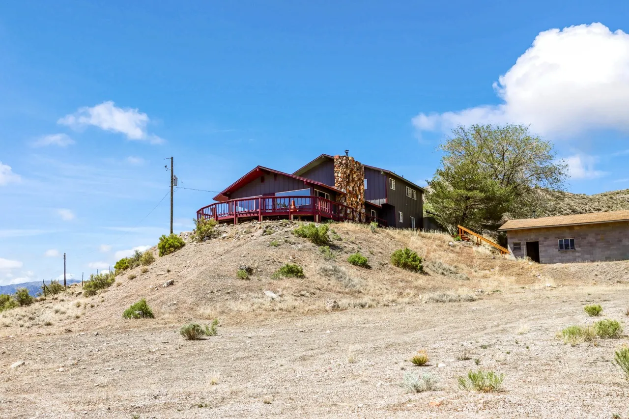 Multi-level residence featuring a stone chimney, wrap-around deck, and an additional detached structure