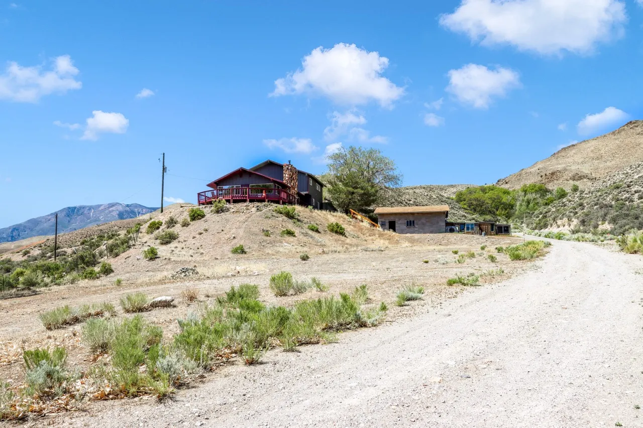 Elevated property with a red-railed deck, stone chimney, and a gravel road approach