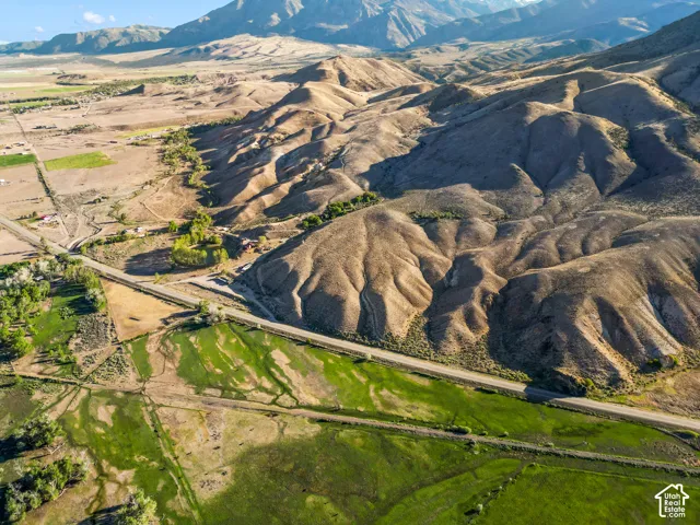 Expansive landscape featuring rolling hills, a winding roadway, diverse terrain, verdant fields, and distant mountains
