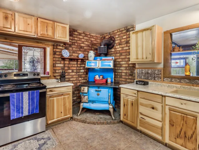 Kitchen featuring light wood cabinetry, light-toned countertops, a stainless steel electric range, and a brick accent wall