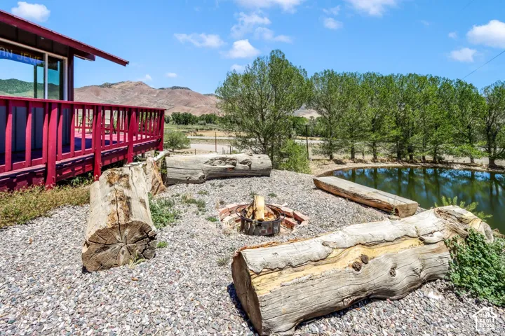 Elevated deck with red railing, gravel ground cover, fire pit, natural log seating, and a water feature surrounded by mature trees