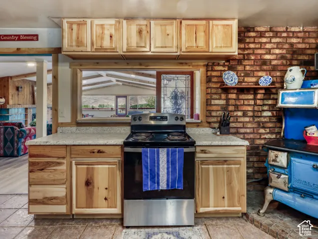 Light wood-finish cabinetry, light-toned countertops, tile flooring, and exposed brick wall detailing