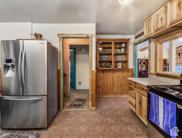 Stainless steel refrigerator, tile flooring, wood-finish cabinetry, built-in display cabinet, and a pass-through window