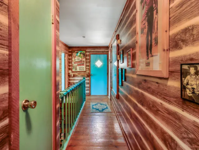 Wood-paneled hallway with wood-finish flooring, a painted baluster, and a painted door