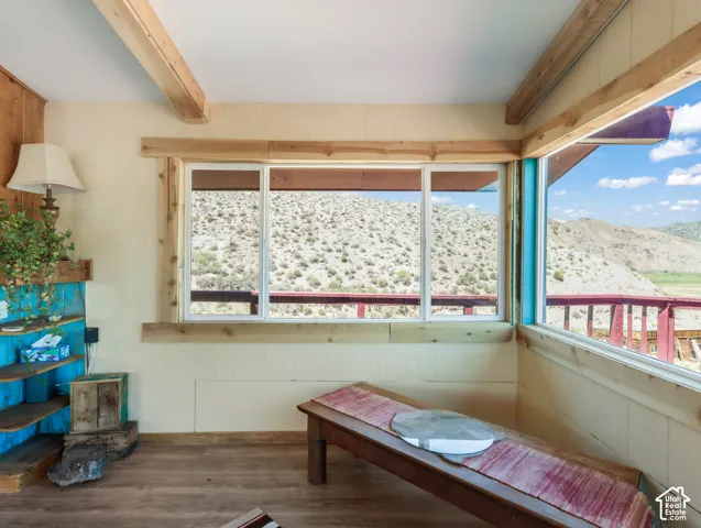 Exposed wood beams, wood-finish flooring, wood trim around windows, built-in shelving unit, and an expansive window with a desert landscape