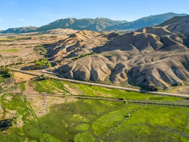 Expansive green fields with a winding road, surrounded by rolling hills and distant mountains under a clear sky