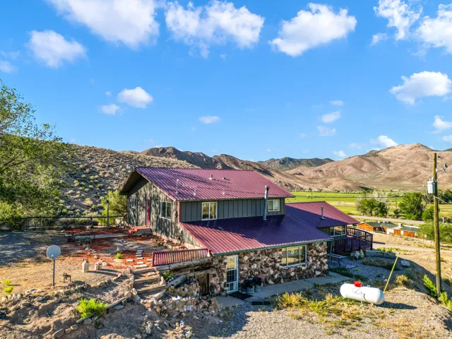 Stone and siding exterior with a red metal roof, featuring multiple decks and a terraced landscape