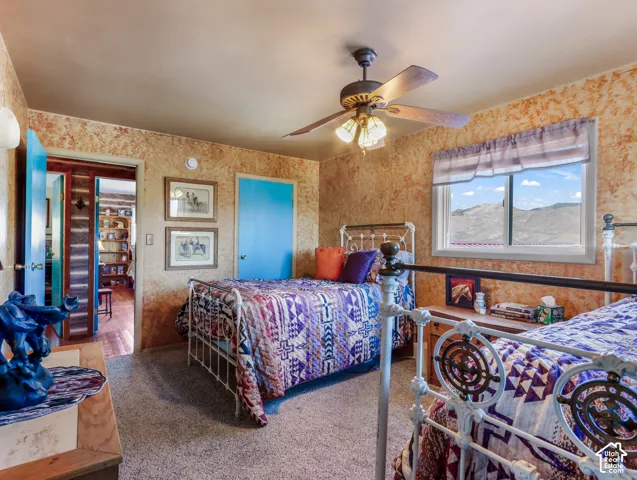 Carpeted room with a ceiling fan, a window with distant scenery, and two beds with decorative metal frames