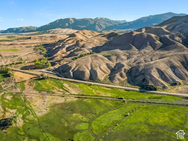 Expansive green fields with a winding road, surrounded by rolling hills and distant mountains under a clear sky