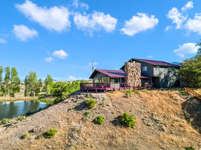 Wood-sided residence with stone chimney accent, featuring a red metal roof and a spacious deck