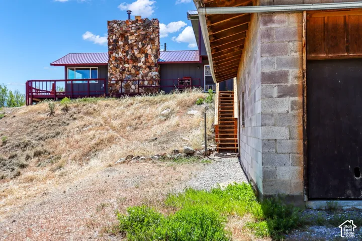 Stone-clad chimney, red metal roof, expansive deck with red railing, and a concrete block structure