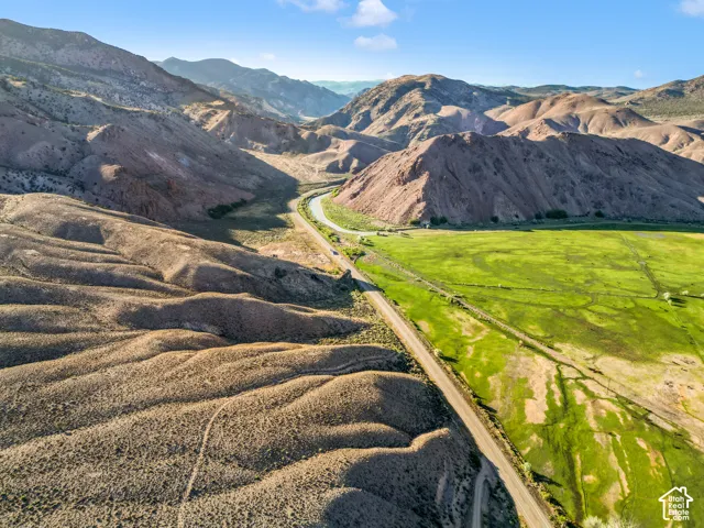 Expansive natural landscape with rolling hills, a winding road, and vibrant green fields, surrounded by rugged mountain terrain