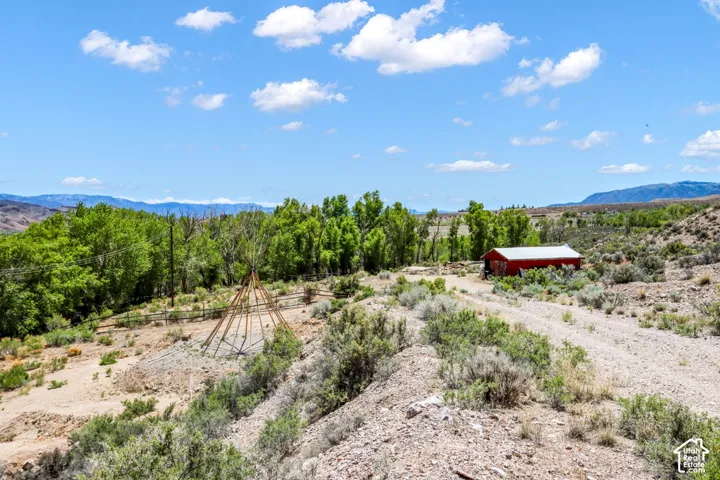 Expansive property featuring a red barn structure, mature trees, mountain range backdrop, and natural landscaping