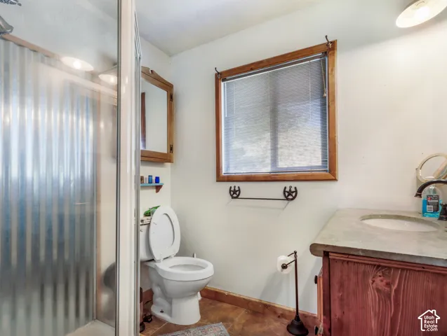 Walk-in shower with corrugated paneling, wood-framed window with blinds, wood-finish vanity with an integrated sink, and wood-finish flooring