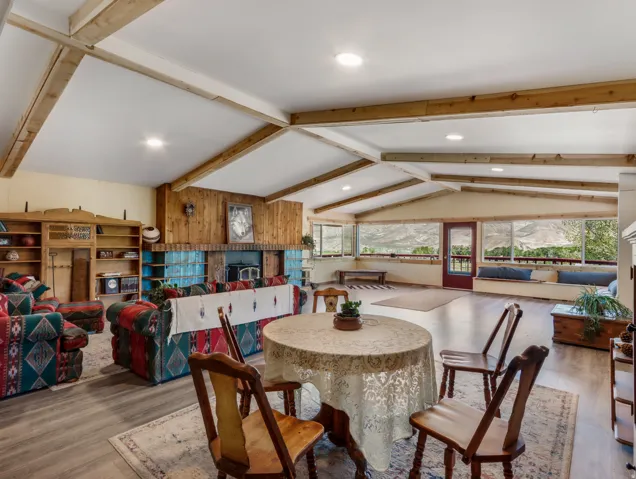 Vaulted ceiling with exposed wood beams, wood-finish flooring, wood-paneled wall, built-in shelving, and a prominent fireplace with a tiled hearth