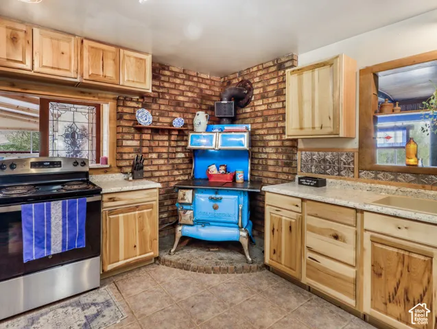 Kitchen featuring light wood cabinetry, light-toned countertops, a stainless steel electric range, and a brick accent wall