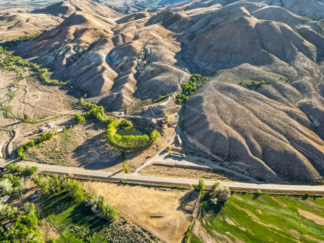 Expansive natural landscape featuring rolling hills, a meandering waterway, a prominent pond, a paved roadway, and green agricultural land