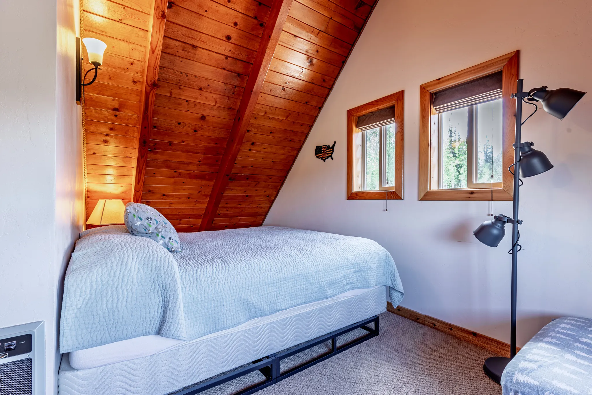 Angled wood-paneled ceiling, white wall finishes, two windows with wood trim, and carpeted flooring