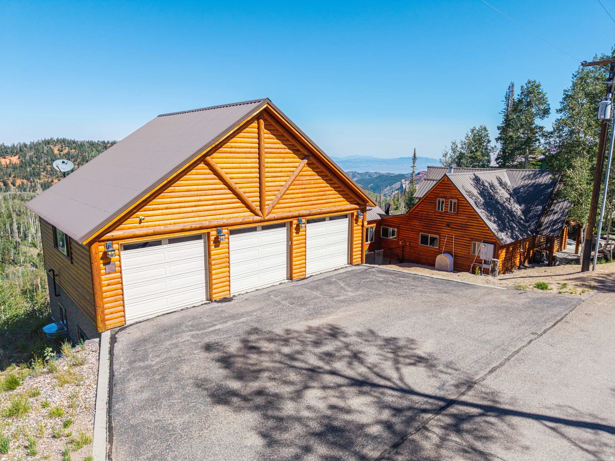 Log-style exterior featuring a three-car garage, gray metal roof, and paved driveway