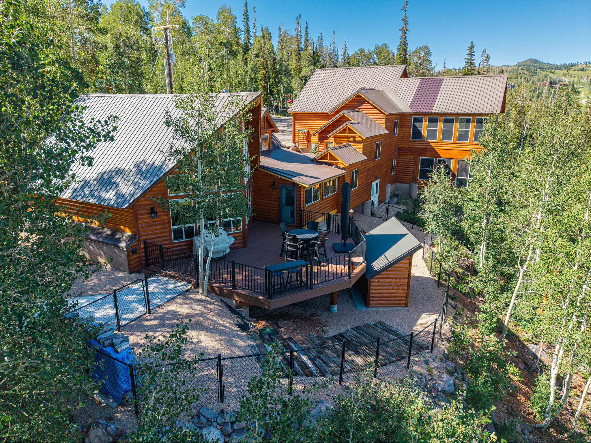Wood-sided exterior featuring multiple structures, a spacious deck, metal roofing, and a gravel perimeter with fencing