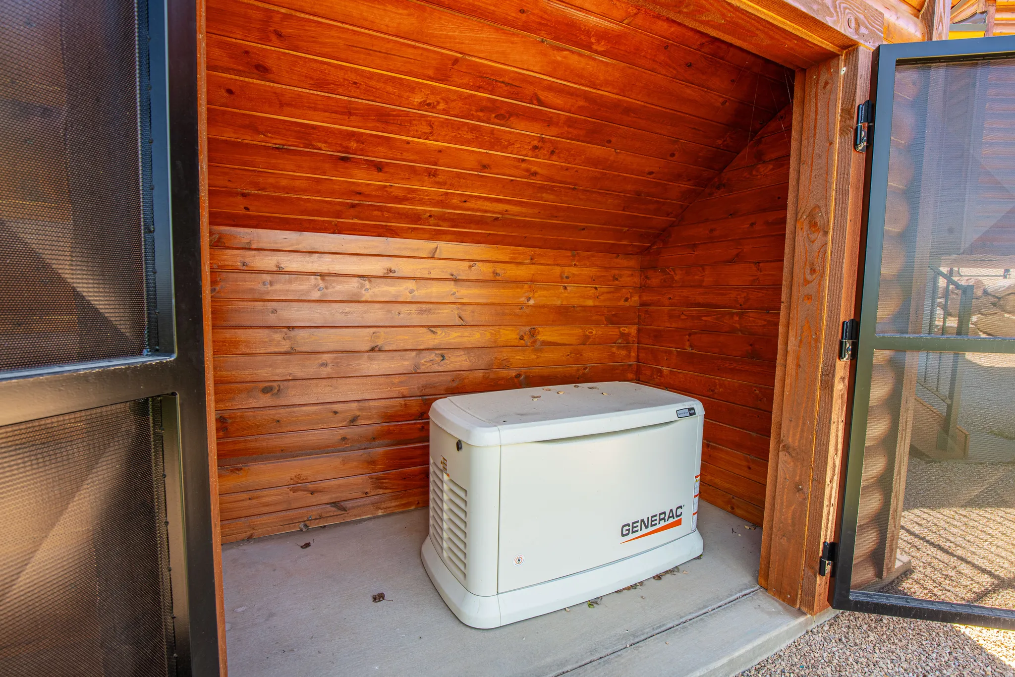 Dedicated utility enclosure with wood paneling, concrete flooring, and a whole-home generator