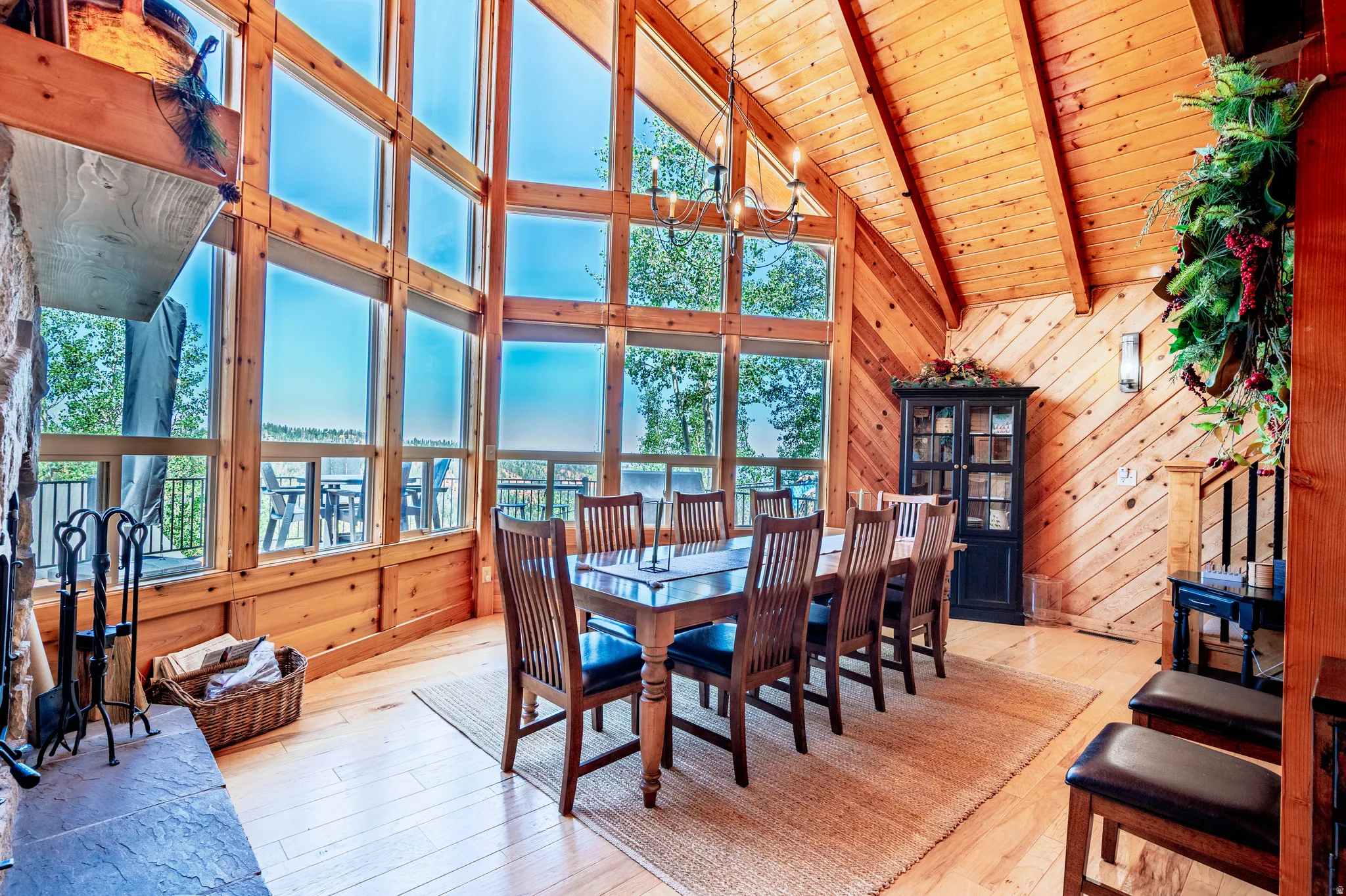 Expansive window wall, vaulted wood-paneled ceiling, wood-finish flooring, stone-clad fireplace with mantel, and built-in display cabinet