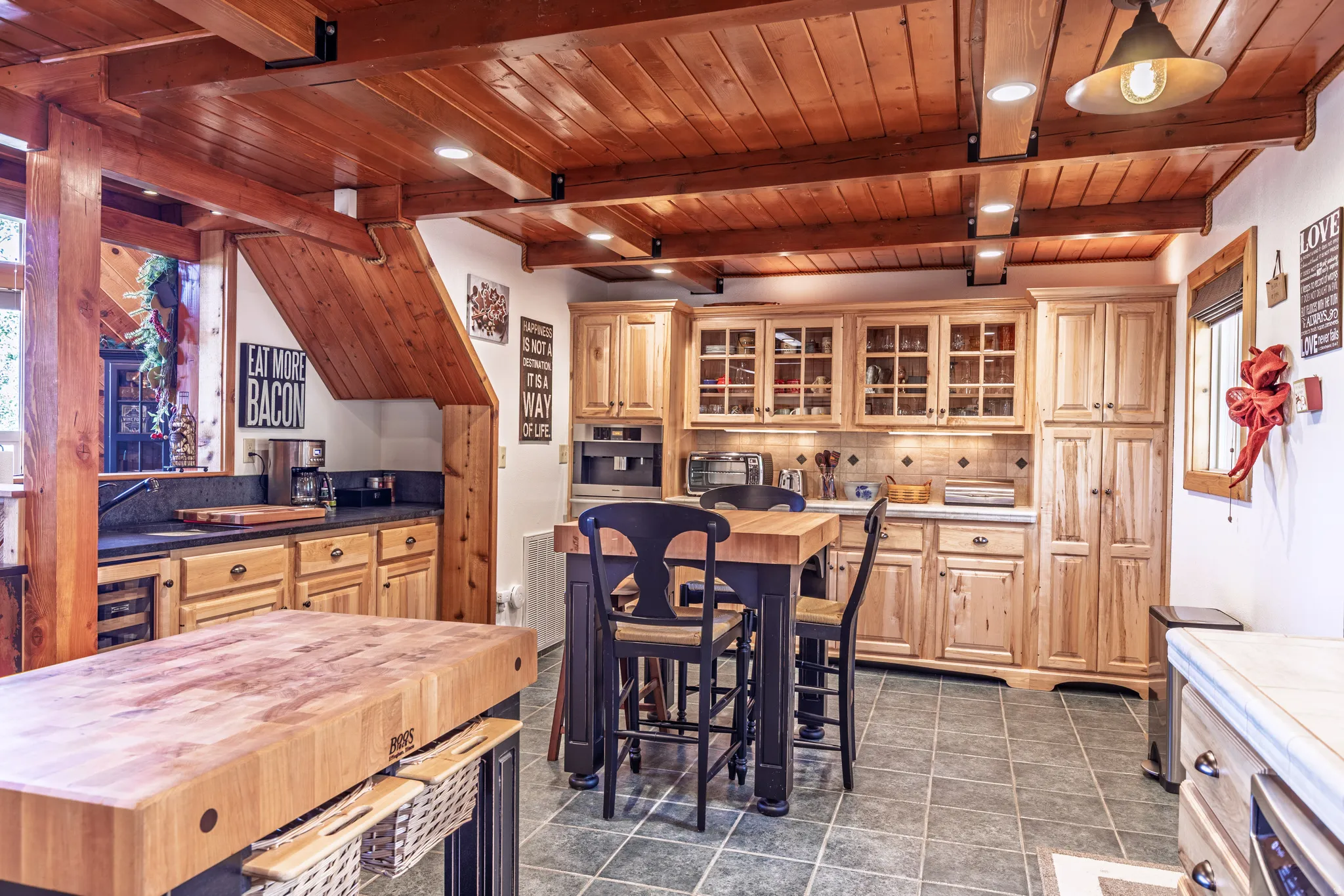 Wood-paneled ceiling with exposed beams, light wood cabinetry, stone countertops, and tile flooring