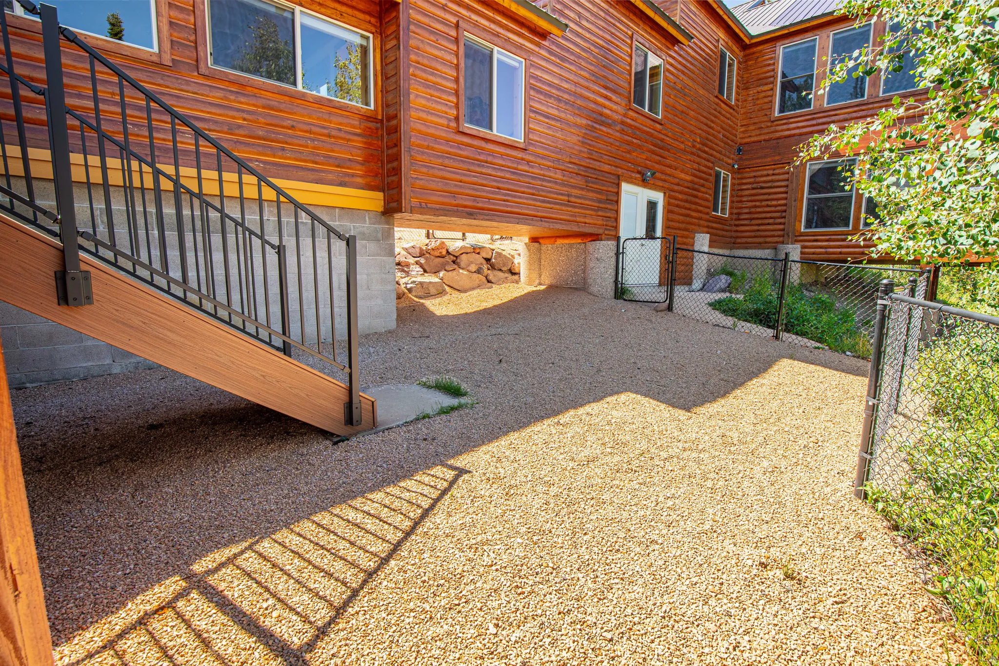 Wood-paneled exterior featuring multiple windows, gravel ground cover, and a black metal fence
