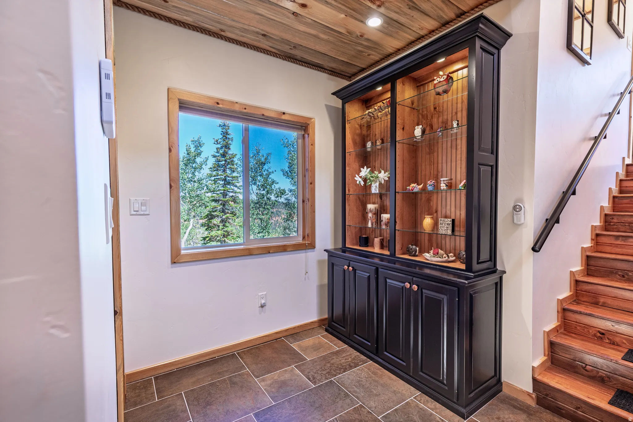Exposed wood ceiling, built-in display cabinet with glass shelving, wood-finish staircase, and tile flooring