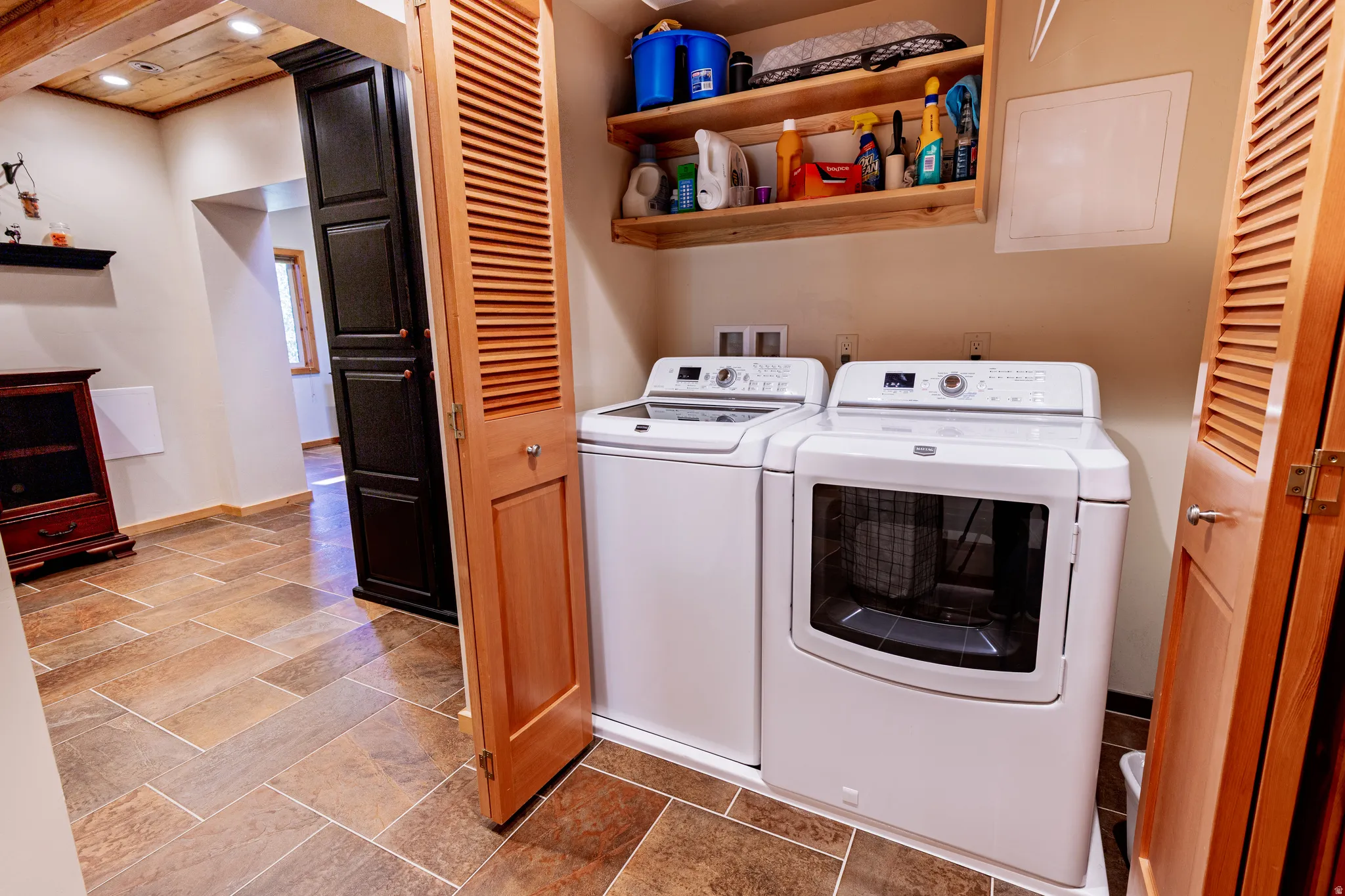 Laundry area with tile flooring, louvered bi-fold doors, and a built-in wood shelf