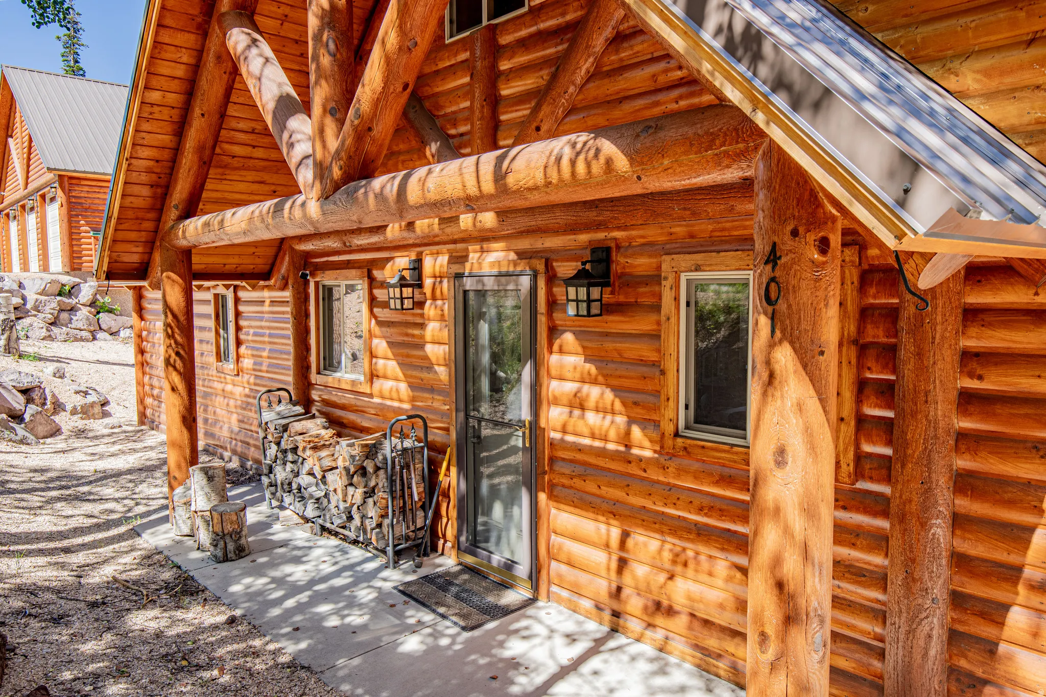 Log cabin construction featuring a covered entry, screened door, and exterior lighting fixtures