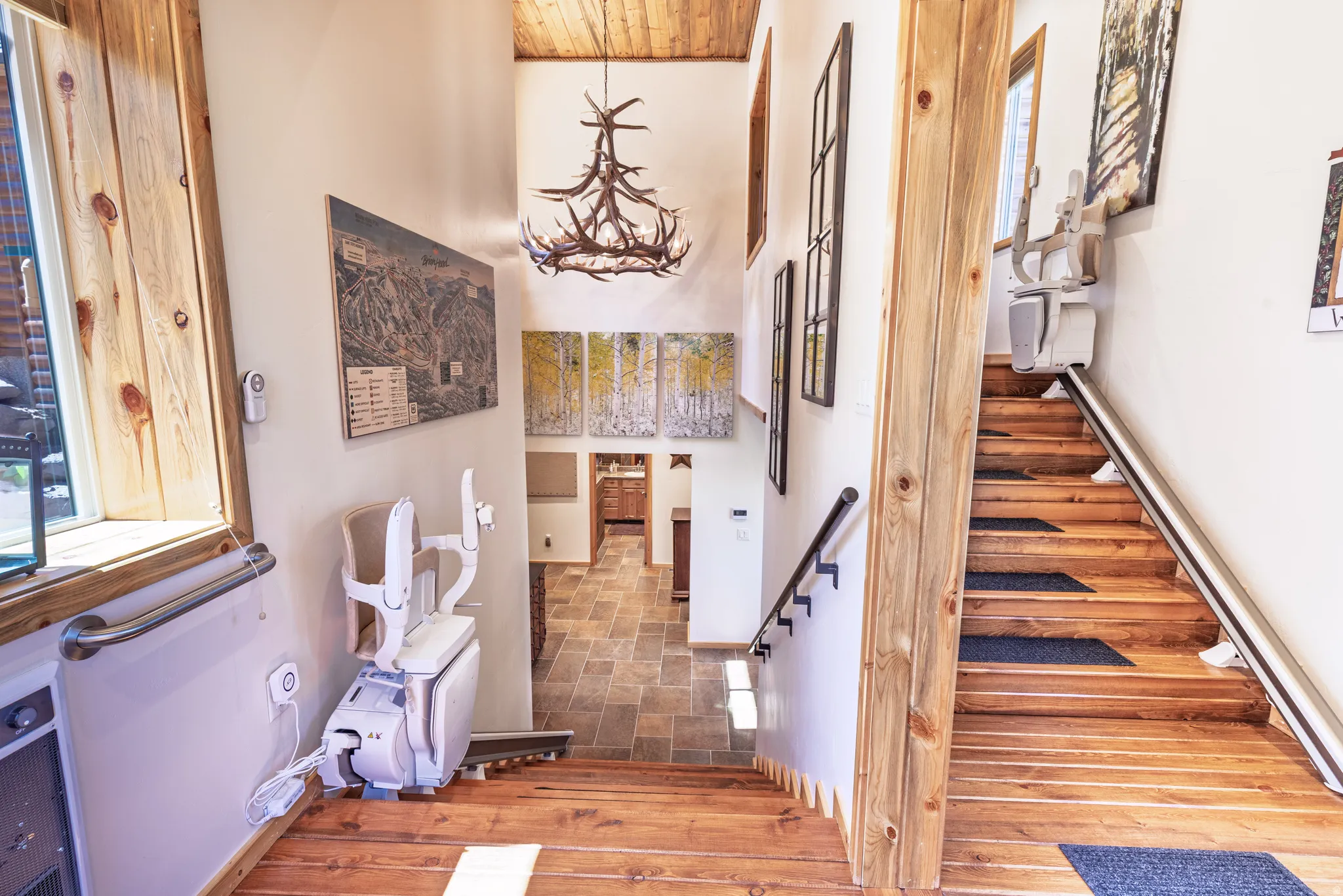 Stone tile flooring, wood-finish stairs, wood-paneled ceiling, ceiling-mounted light fixture, and permanent stair lift installations