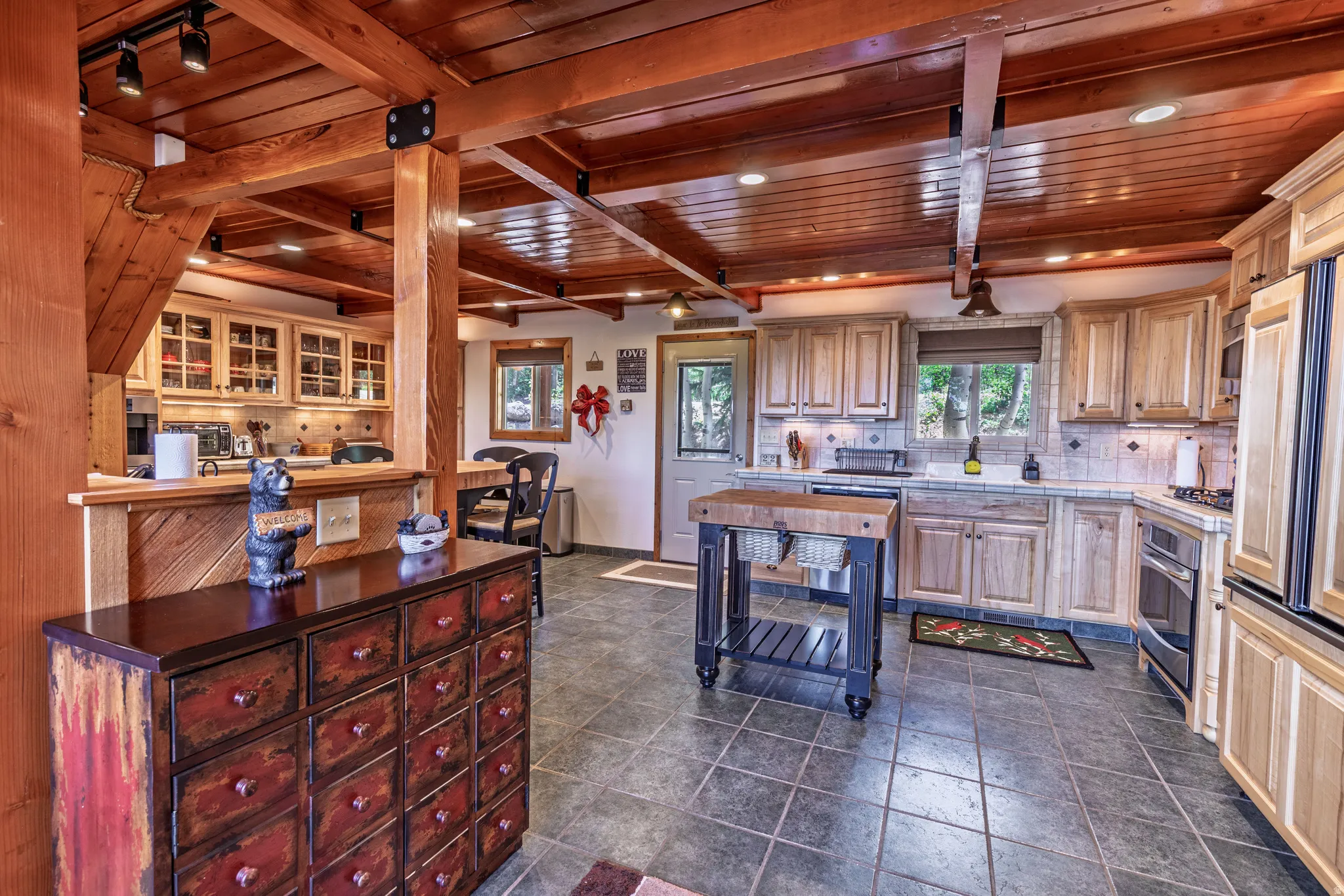 Exposed wood beam ceiling, track lighting, wood-finish cabinetry, tile flooring, and a tile backsplash